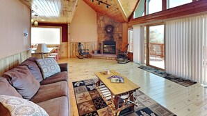 Un salon spacieux avec un plafond en bois, une cheminée en pierre, une grande fenêtre et un balcon.