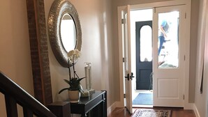 A hallway with a wooden floor, a patterned rug, a mirror, and a door leading outside. - Cozy studio with AC and WiFi in Historic Geneva, NY.  (Geneva)