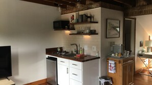 A compact kitchen with white cabinetry, a stainless steel dishwasher, a microwave, and a sink. There is a wooden countertop with a kettle and a small trash bin. - Cozy studio with AC and WiFi in Historic Geneva, NY.  (Geneva)