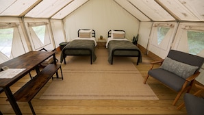Een tent met twee bedden, een houten tafel en een stoel.