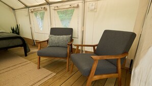Een tent met twee houten stoelen, een bed en een raam met uitzicht op het bos.