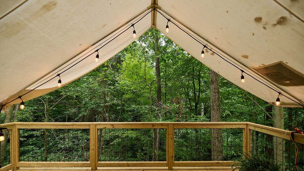Een houten terras met een leuning, sfeerverlichting en uitzicht op een bos.