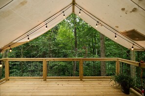 A wooden deck with a railing, string lights, and a view of a forest. - Valley Overlook, Peninsula, Ohio - Glamping Tent P7 (Akron)