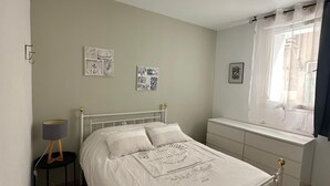 Un dormitorio con cama, mesita de noche, lámpara y una obra de arte en la pared.