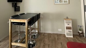 Una habitación pequeña y moderna con una mesa de madera, sillas, un televisor montado en la pared, un cuadro enmarcado y un mueble pequeño.