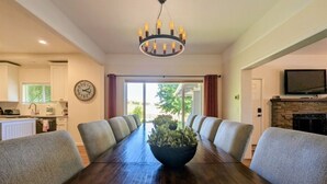 A dining room with a long wooden table, grey upholstered chairs, a central plant, and a chandelier. - Wine Country Farmhouse with Gourmet Kitchen. Perfect for Large Groups. (Dayton)