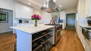 A modern kitchen with white cabinetry, a central island, stainless steel appliances, and a decorative vase of flowers. - Wine Country Farmhouse with Gourmet Kitchen. Perfect for Large Groups. (Dayton)