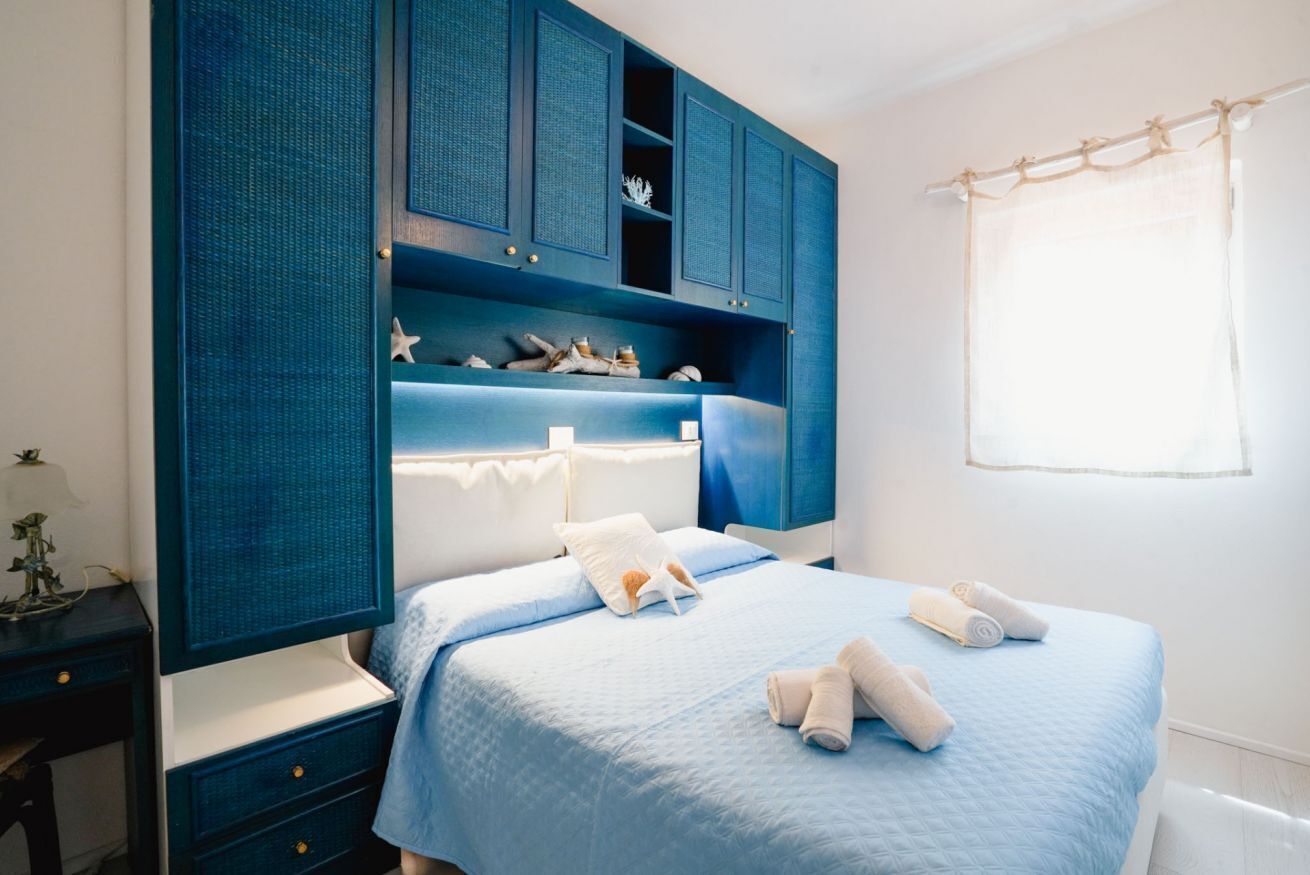 Une chambre à coucher avec un lit, une table de chevet, une commode et une fenêtre avec des rideaux.