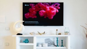 A white entertainment center with a flat-screen TV displaying a pink abstract image. - Palau | Bella Vista Apartment | vista mare e terrazzo (Palau)