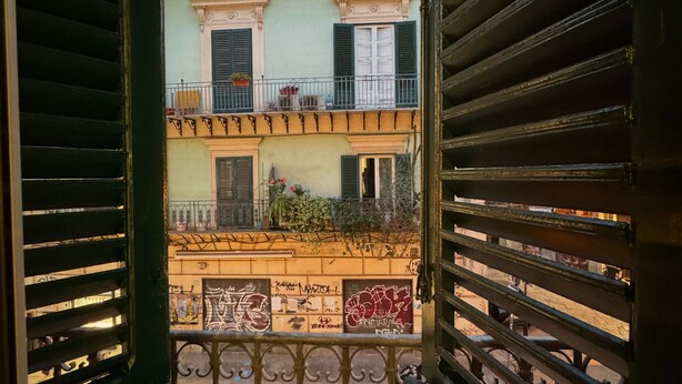 Une vue à travers un balcon orné de barreaux en métal, donnant sur un immeuble doté de nombreux balcons et dont le sol est recouvert de carreaux.