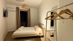Une petite chambre à coucher moderne, avec un lit, une lampe de chevet, un banc en bois, un tapis rond et un porte-vêtements.