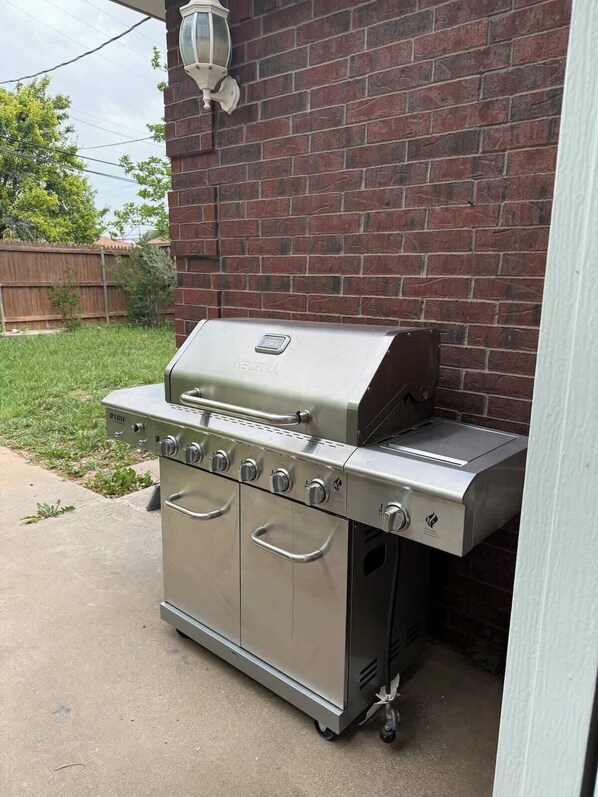 Una parrilla de acero inoxidable para exteriores con quemador lateral y chimenea, ubicada frente a una pared de ladrillo.