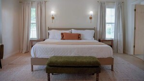 A spacious bedroom with a large bed, two bedside tables, and a bench. - 4BR Sleep 12 | Family, Corp Stays | Palo Duro Cyn (Amarillo)