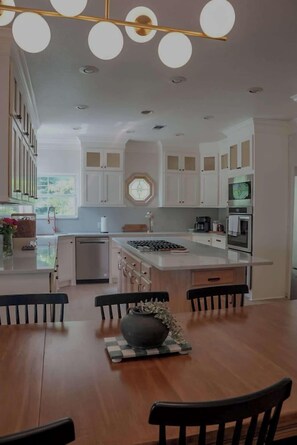 Una cocina moderna con armarios blancos, una isla central y un comedor con mesas y sillas de madera.