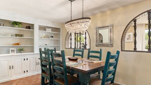 A dining area with a wooden table, teal chairs, a chandelier, and white cabinets with shelves. - Spacious Tubac Escape – 4BR/3BA, Private Pool, Bar, Workout Room & 2 King Suites (Tubac)