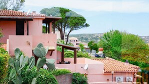 Un edificio rosa con techo de tejas, un patio cubierto y vistas a una colina verde.