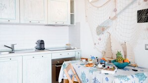 Una cocina con armarios blancos, una cafetera y una mesa con fruteros y un libro.