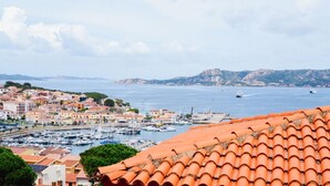 Un pueblo costero con un puerto deportivo, tejados de teja rojiza y montañas al fondo.