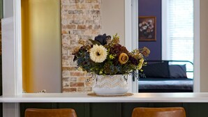 A kitchen with a brick accent wall, a white vase with flowers, two brown bar stools, and a hanging light fixture. - Stillwater's Enchanted Escape (Stillwater)