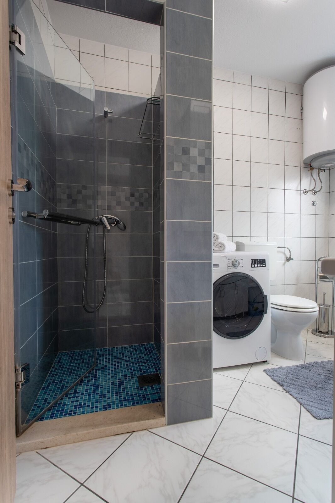 Un baño moderno con ducha a ras de suelo, lavadora e inodoro.