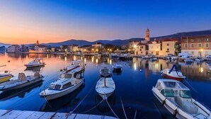 En lysthavn med både i havnen om natten, omgivet af bygninger og et bjerg i baggrunden.
