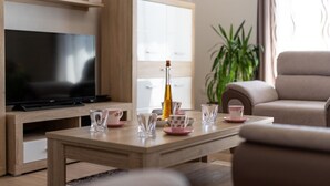 En moderne stue med et fladskærms-tv, et træsofabord med pyngegenstande, en beige sofa og en potteplante.