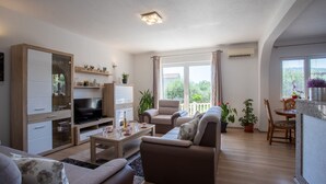 En rummelig stue med sofa, lænestole, et fjernsyn og et spisebord med stole.