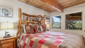 A bedroom with a wooden headboard, a quilted bedspread, and a view of the outdoors through a window. - Wolf View Lodge (Big Bear City)