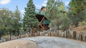 A rustic wooden staircase leading to a cabin with a green roof, surrounded by trees and a wooden fence. - Wolf View Lodge (Big Bear City)