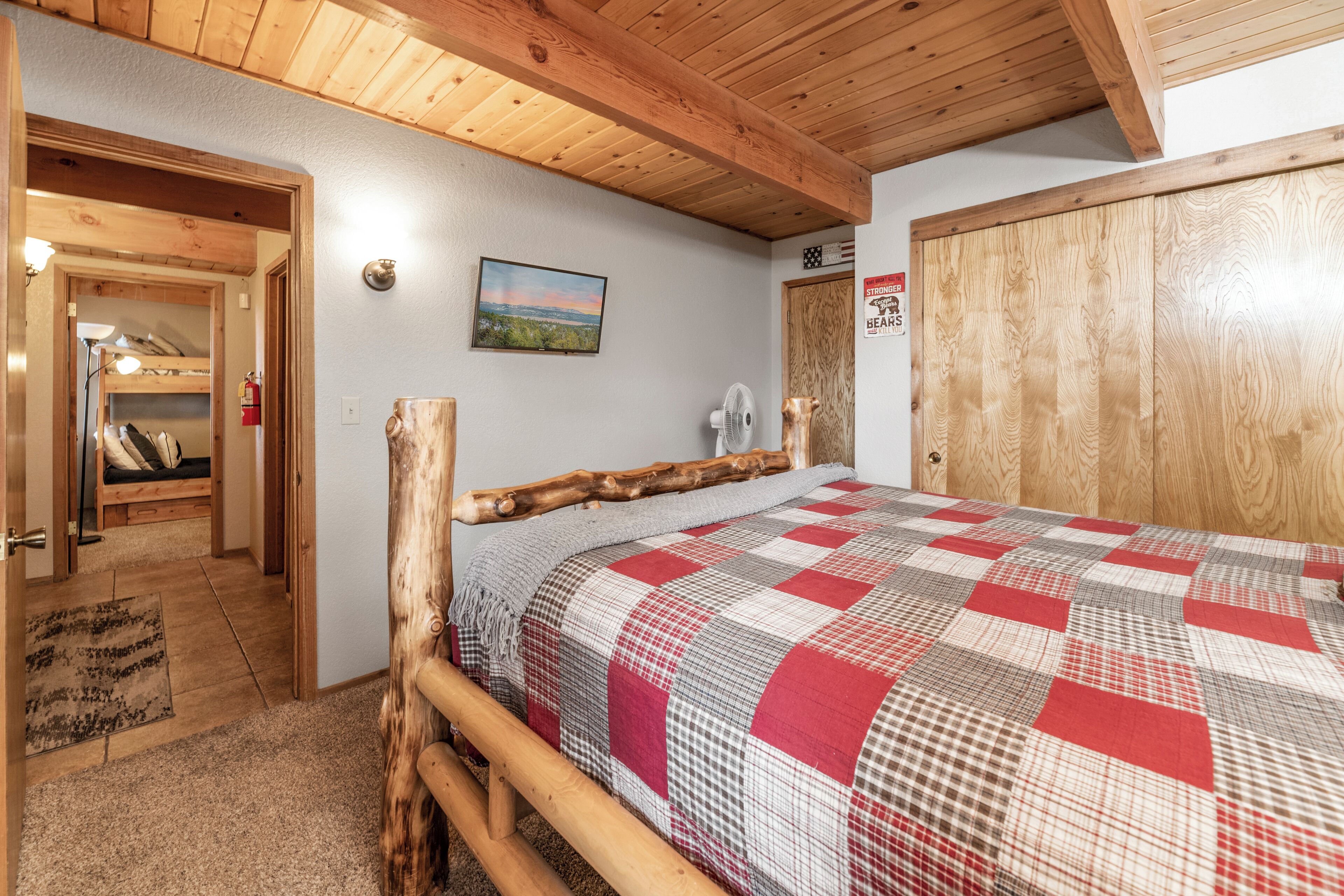 Een slaapkamer met een houten bedframe, een geruit beddegoed, een schilderij aan de muur en een houten garderobe.