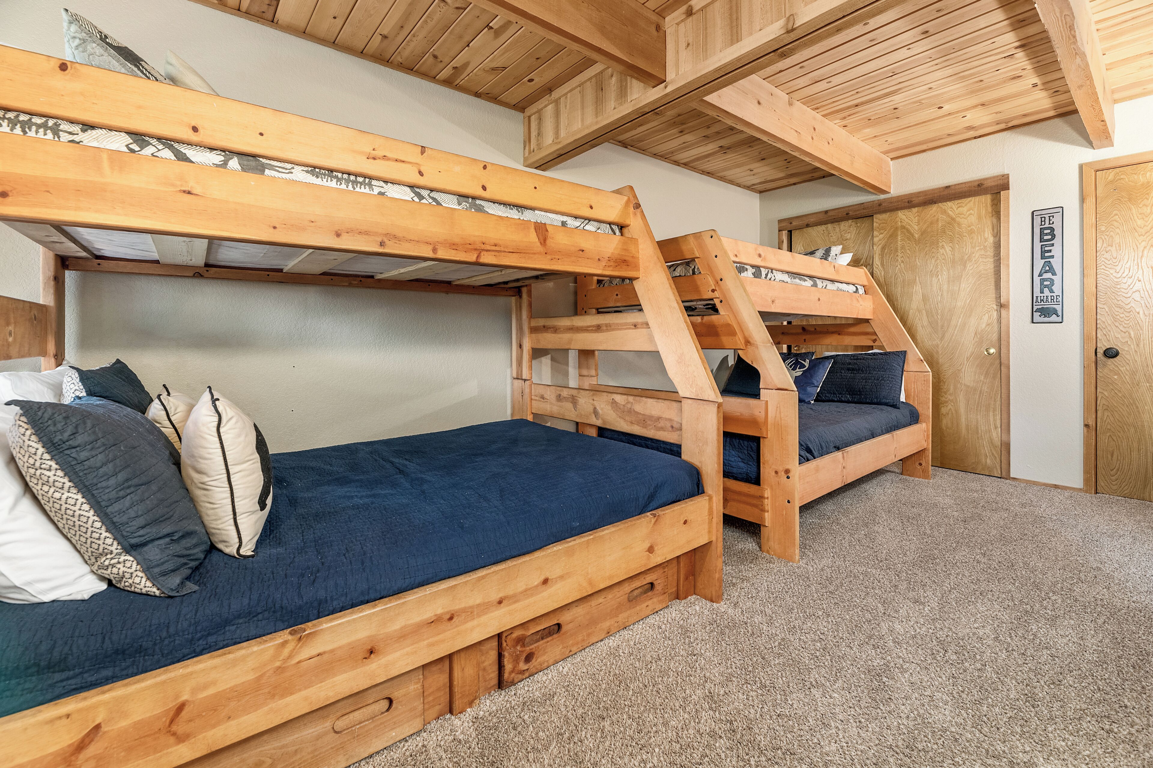 Una habitación con dos literas, vigas de madera en el techo, una puerta con un letrero y suelo cubierto de alfombra.
