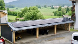 Un garatge cobert amb panells solars, motos aparcades i un cotxe.