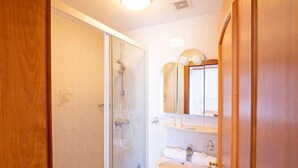 Un bany amb una cabina de dutxa de vidre, un lavabo amb un mirall a sobre i una porta de fusta.