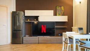 Ett modernt kök med en inbyggd TV som visar Netflix-logotypen, ett kylskåp och en matplats med ett vitt bord och stolar.