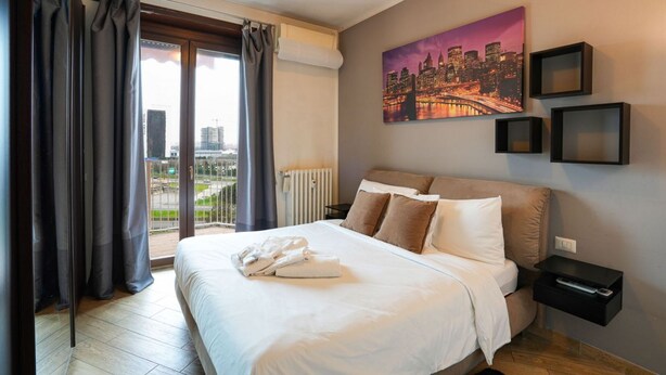 Ett hotellrum med en stor säng, en målning som föreställer stadens silhuett och utsikt över staden genom fönstret.