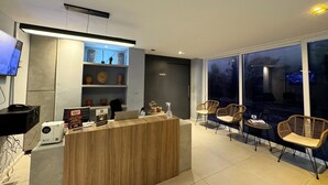Un área de recepción moderna con un mostrador de madera, estantes con objetos decorativos y sillas de mimbre.