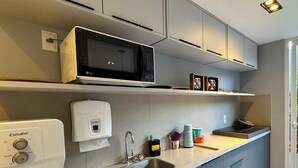 Una cocina moderna con microondas integrado, dispensador de agua, fregadero y un calentador de agua Esmaltec compacto.