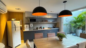 Una cocina moderna con refrigerador, microondas y lavamanos. Hay una mesa de comedor con sillas y una planta en maceta.