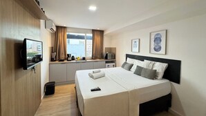 Una habitación de hotel con cama, televisión, kitchenette y ventana con cortinas.
