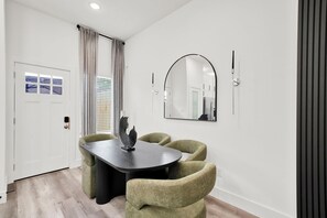 Un espace repas moderne avec une table sombre, quatre chaises vertes, une sculpture décorative et un grand miroir au mur.