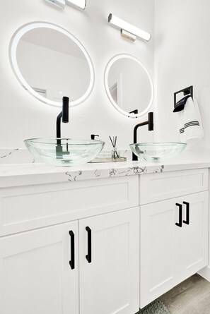 Une salle de bain moderne avec deux vasques en verre, des robinets noirs et des meubles blancs.