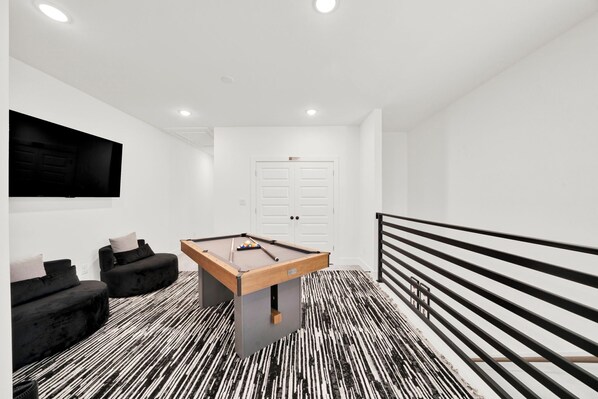 Une pièce moderne avec une table de billard, des canapés noirs et un tapis rayé noir et blanc.