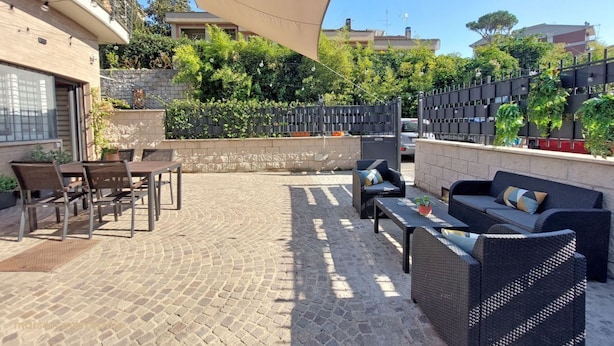 An outdoor patio with a table and chairs, a sofa, and a large umbrella providing shade.