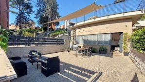 An outdoor patio area with a table and chairs, a sofa, and a large umbrella providing shade.