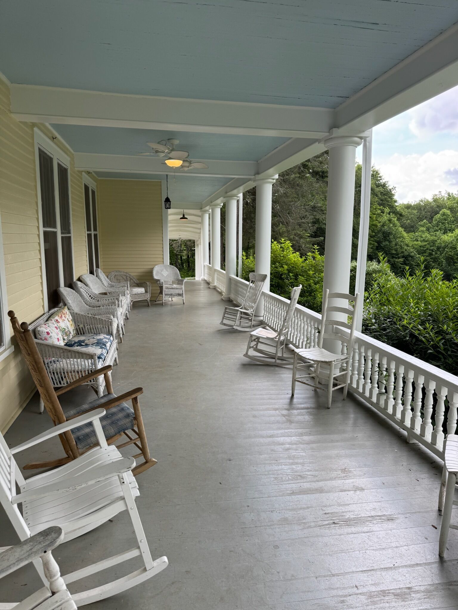 Eine überdachte Veranda mit weißen Korbmöbeln, Säulen und Blick ins Grüne.