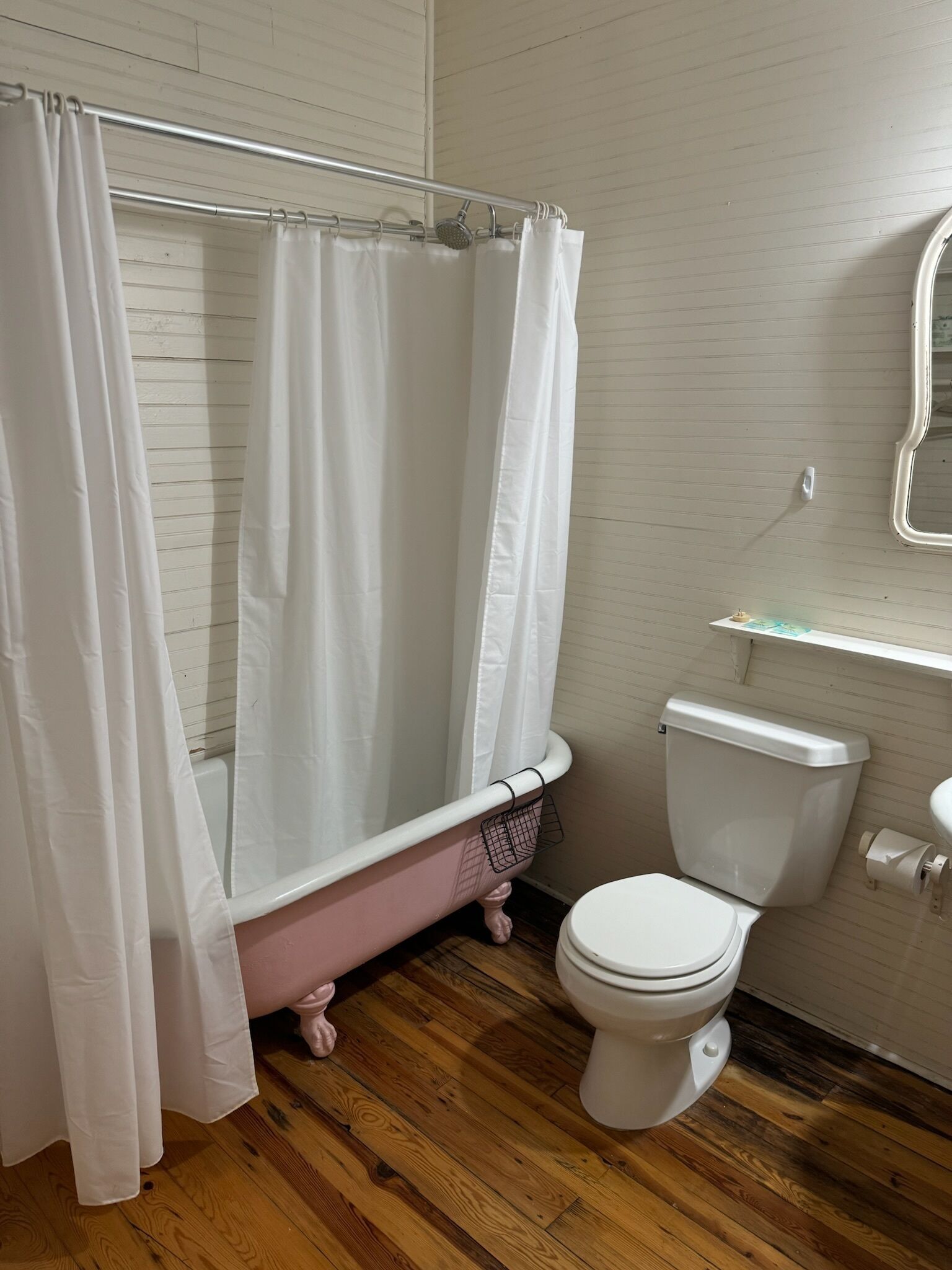 Ein Badezimmer mit Holzboden, einer weißen Toilette und einer Badewanne mit Füßen in Rosa.