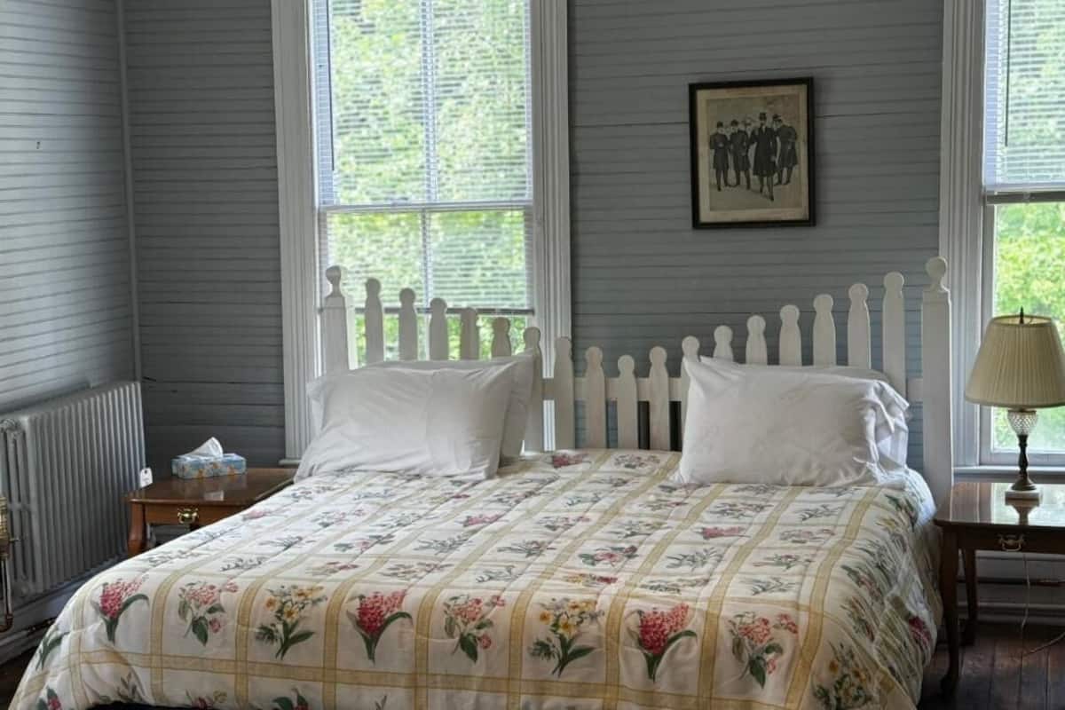 A bedroom with a bed, a nightstand, a lamp, and a window with blinds.
