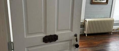 A white door with a handle and a keyhole, a radiator, and a framed picture on the wall.