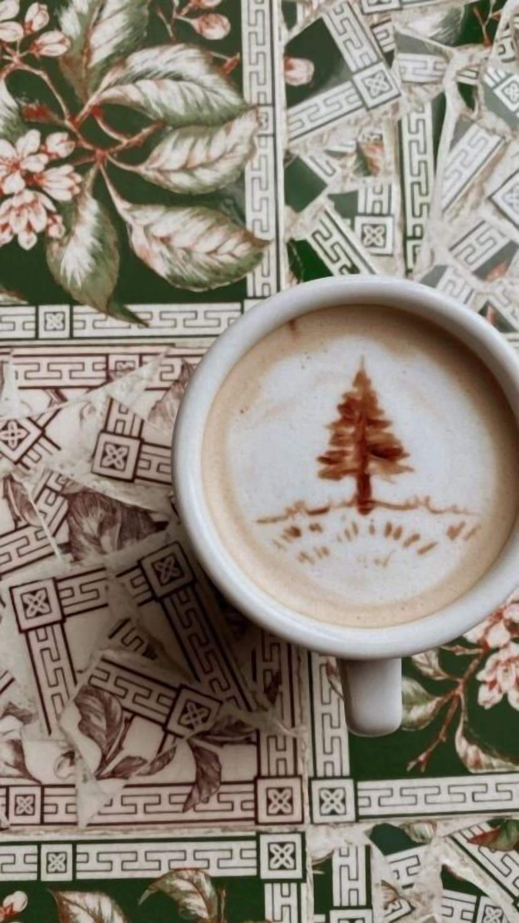 A cup of coffee with a latte art of a tree on a patterned tablecloth.