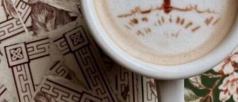 Une tasse de café sur laquelle on a réalisé un motif en latte art représentant un arbre, le tout posé sur une nappe à motifs.